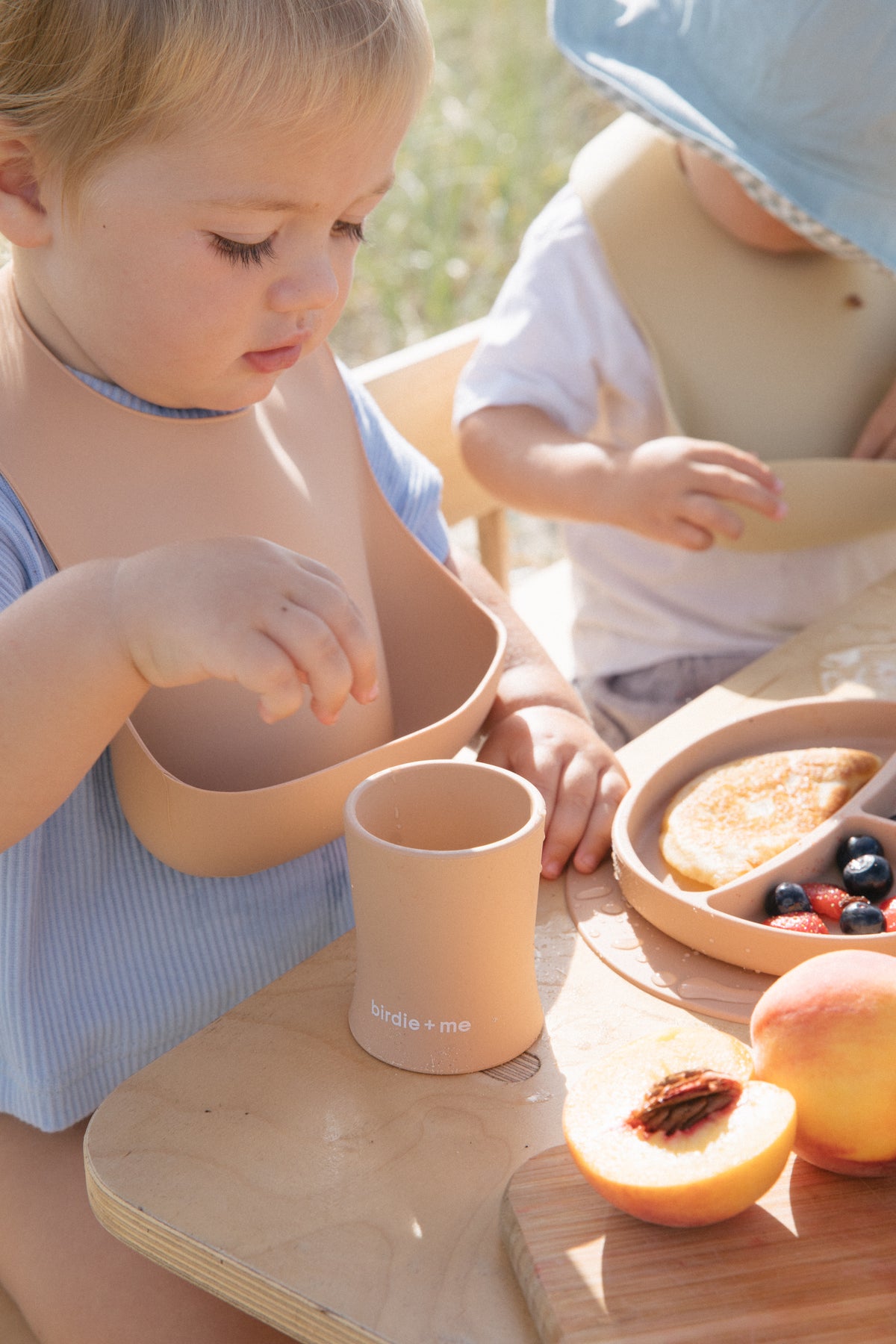 Silicone bib in blush worn by toddler.